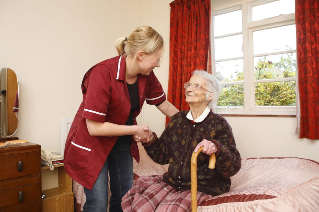 Elderly woman receiving aid for sitting and standing with caregiver support