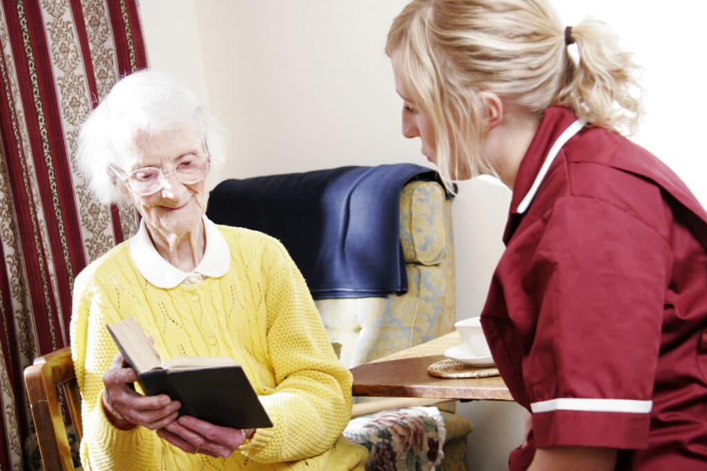 Caregiver companing with elderly patient holding a book