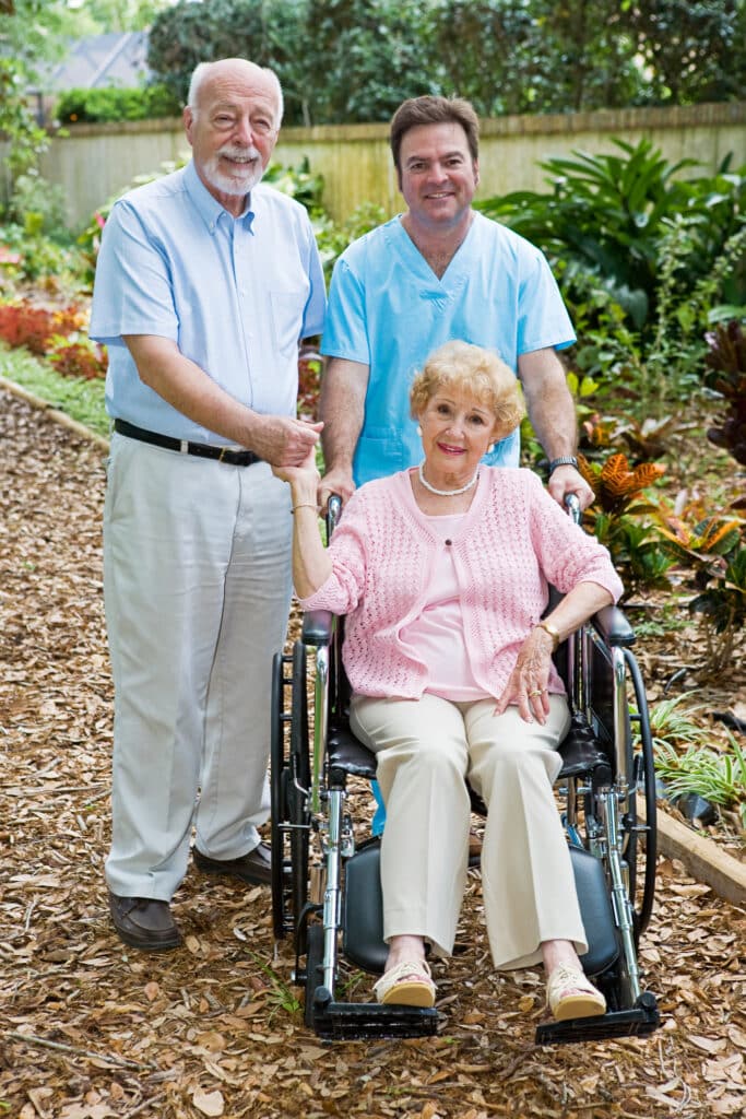 Supportive nurse guiding wheelchair for elderly couple