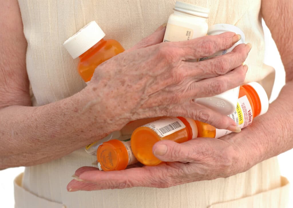 Elderly person clutching medicine bottles