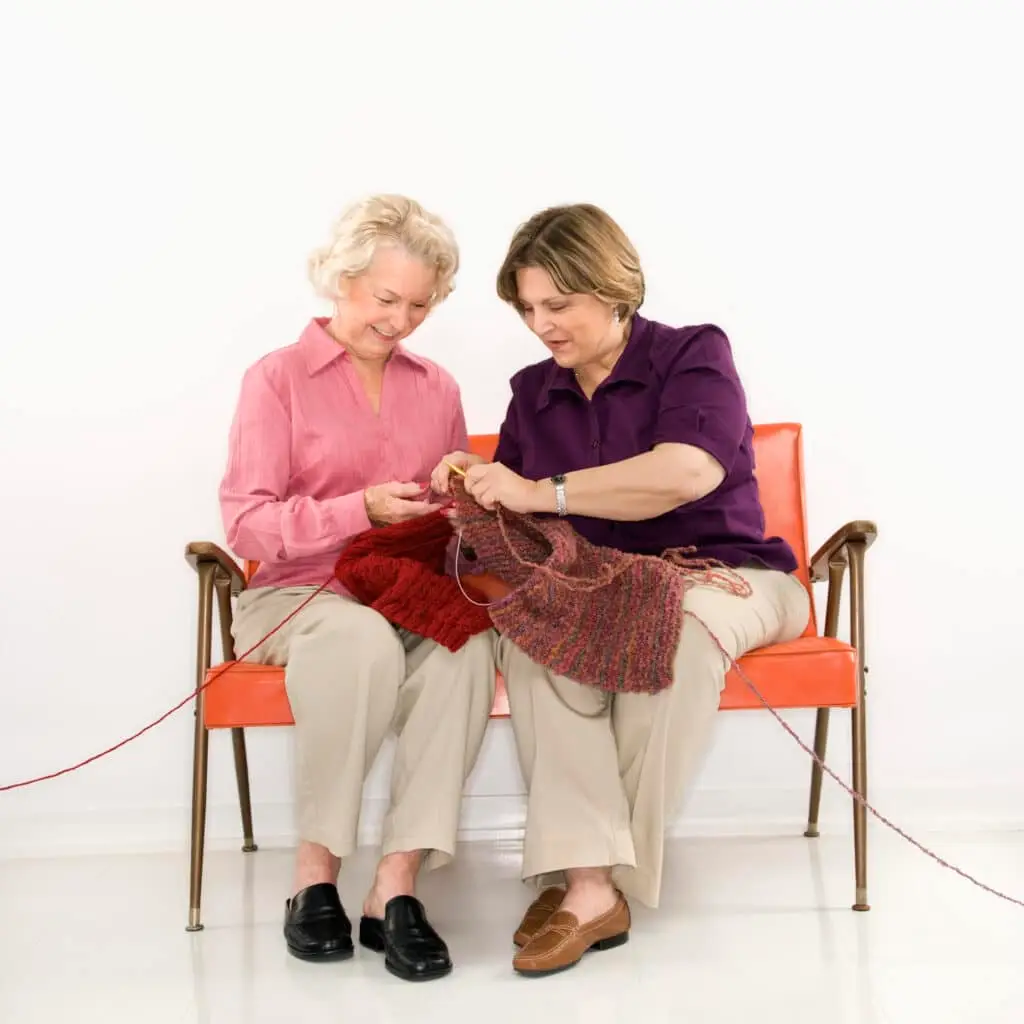 Caucasian middle aged woman and senior woman sitting and knitting.